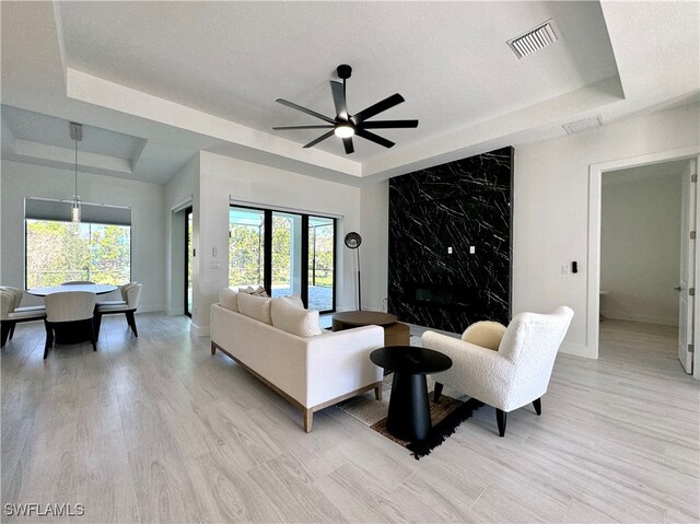 living room featuring a raised ceiling, ceiling fan, and light hardwood / wood-style floors