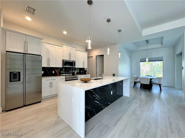 kitchen with pendant lighting, white cabinetry, stainless steel appliances, and an island with sink