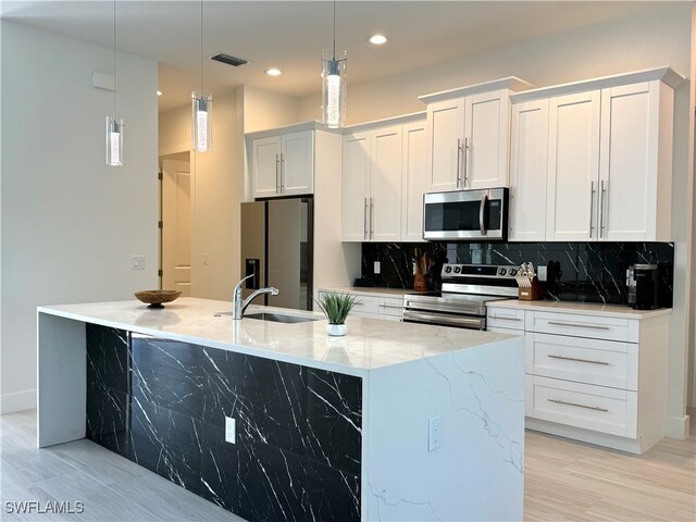 kitchen featuring light wood-type flooring, stainless steel appliances, a kitchen island with sink, white cabinetry, and hanging light fixtures