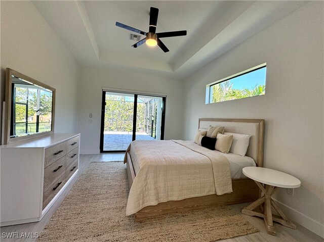 bedroom with access to outside, multiple windows, a tray ceiling, and ceiling fan