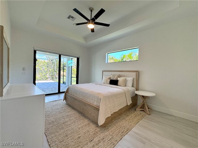 bedroom featuring a tray ceiling, access to exterior, ceiling fan, and light hardwood / wood-style flooring