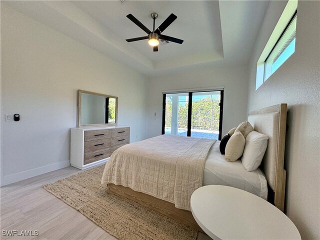 bedroom featuring a tray ceiling, access to exterior, ceiling fan, and light hardwood / wood-style floors