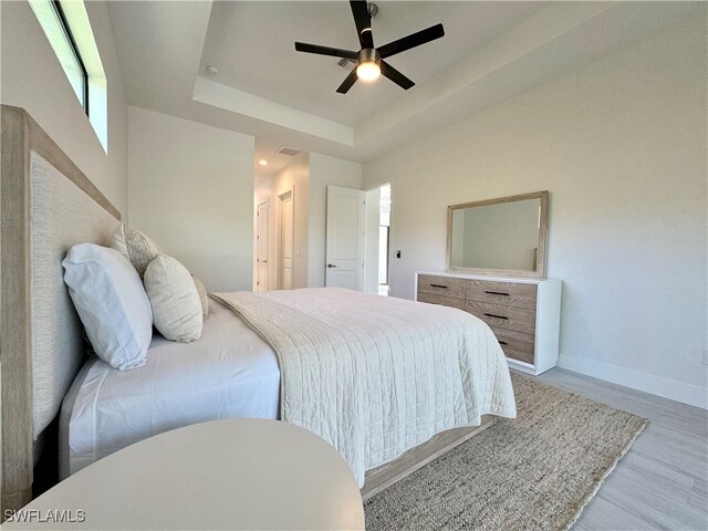 bedroom featuring light wood-type flooring, a tray ceiling, and ceiling fan