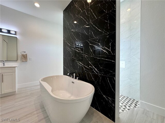 bathroom featuring plus walk in shower, wood-type flooring, vanity, and tile walls