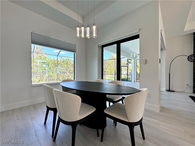 dining space with a raised ceiling, a chandelier, and light hardwood / wood-style floors