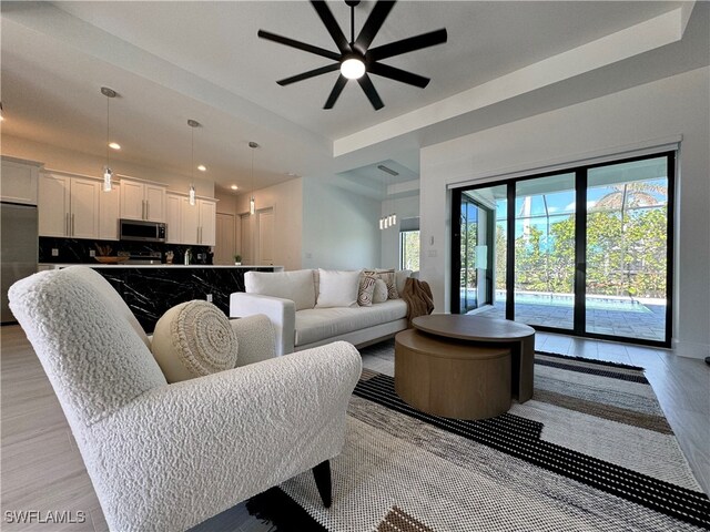 living room with ceiling fan, light hardwood / wood-style floors, and a tray ceiling