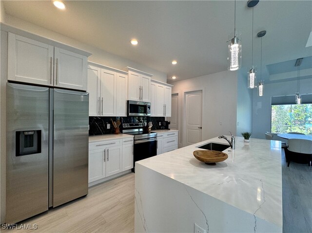 kitchen with decorative backsplash, appliances with stainless steel finishes, sink, white cabinets, and hanging light fixtures