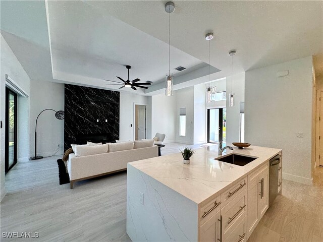 kitchen featuring light stone countertops, dishwasher, sink, hanging light fixtures, and an island with sink