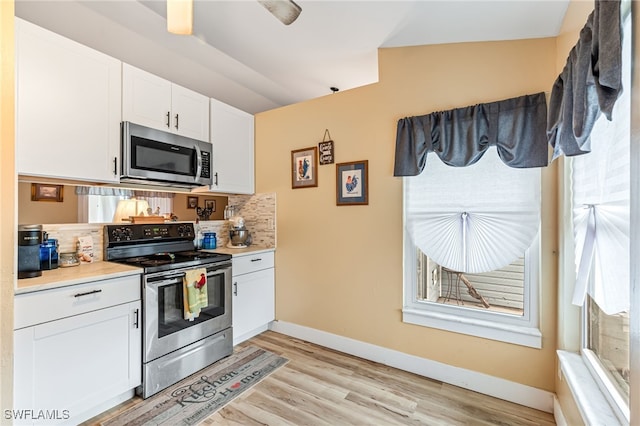 kitchen featuring tasteful backsplash, stainless steel appliances, light hardwood / wood-style floors, white cabinetry, and lofted ceiling