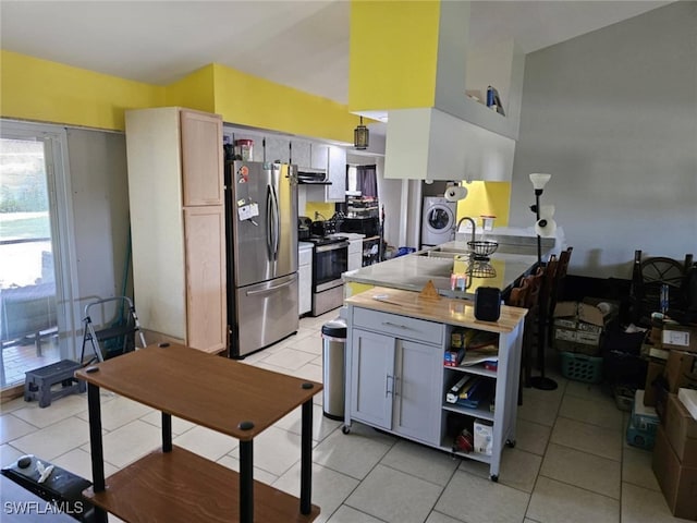 kitchen with washer / dryer, kitchen peninsula, light tile patterned floors, and appliances with stainless steel finishes