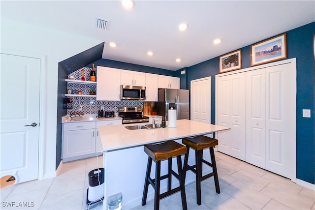 kitchen with a kitchen island with sink, a kitchen breakfast bar, tasteful backsplash, white cabinetry, and stainless steel appliances