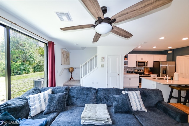 living room featuring beam ceiling, ceiling fan, and sink