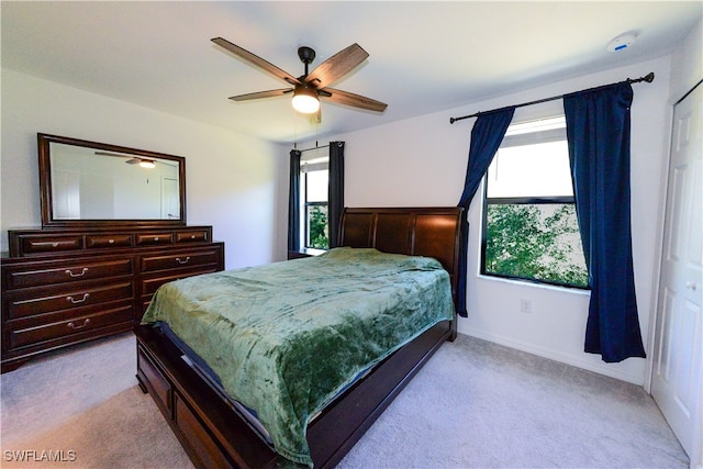 bedroom featuring multiple windows, ceiling fan, a closet, and light carpet