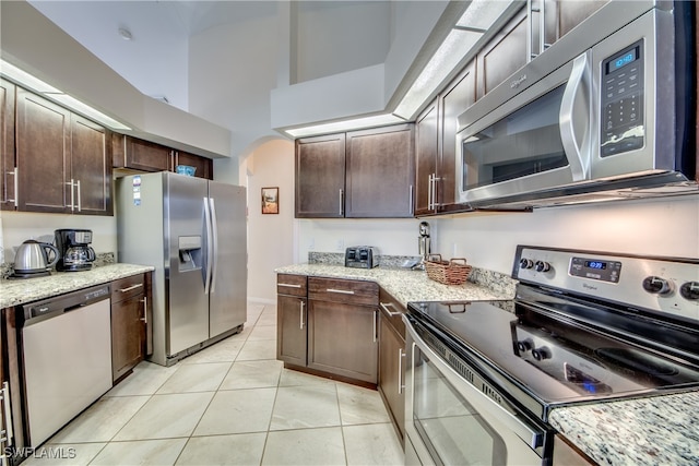 kitchen with dark brown cabinetry, light stone counters, light tile patterned flooring, and stainless steel appliances