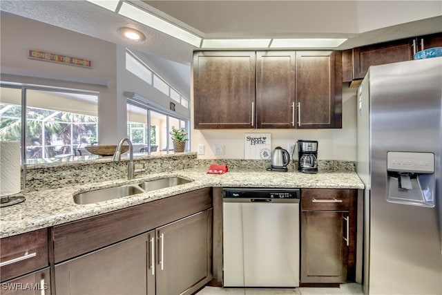 kitchen with dark brown cabinets, stainless steel appliances, light stone counters, and sink