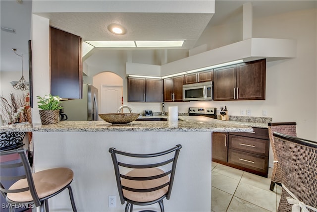 kitchen featuring a kitchen bar, dark brown cabinetry, stainless steel appliances, and light stone counters