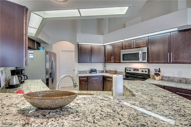 kitchen featuring dark brown cabinets, light stone countertops, kitchen peninsula, and appliances with stainless steel finishes