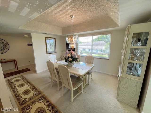 dining room featuring light carpet, a textured ceiling, a chandelier, and a raised ceiling