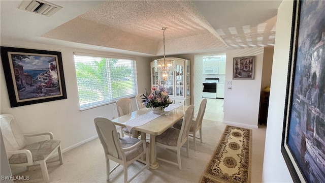 carpeted dining area with a raised ceiling, a textured ceiling, and a notable chandelier