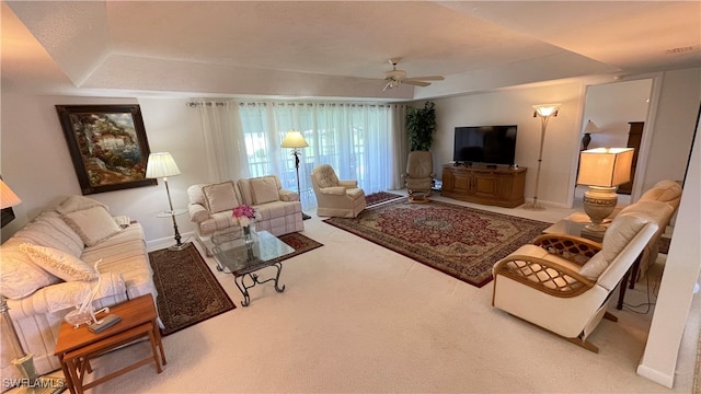 living room featuring a raised ceiling, ceiling fan, and light carpet