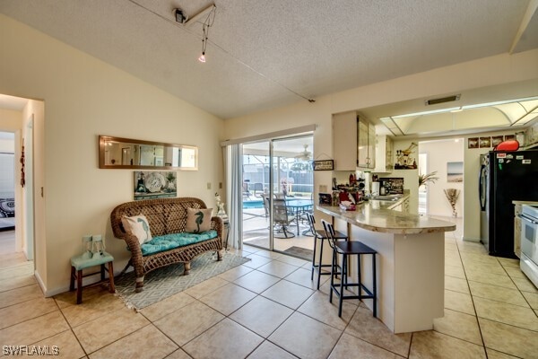 kitchen featuring kitchen peninsula, light tile patterned floors, black refrigerator, and a breakfast bar area