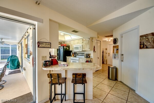 kitchen with kitchen peninsula, white appliances, ceiling fan, light tile patterned floors, and a breakfast bar area