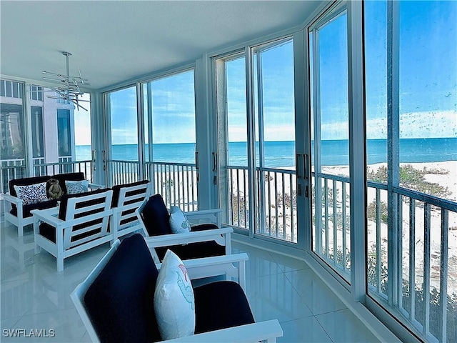 sunroom featuring a beach view, a water view, and an inviting chandelier