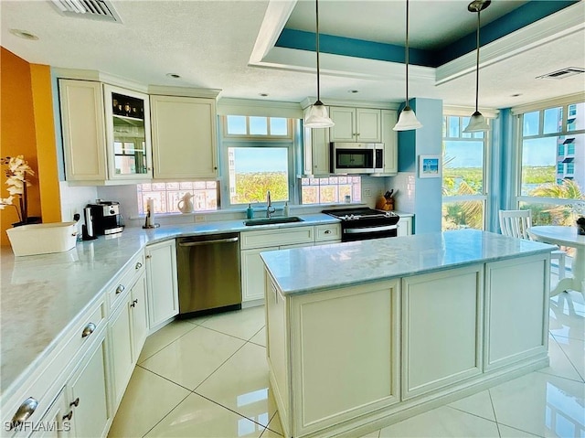 kitchen featuring a raised ceiling, hanging light fixtures, a kitchen island, light stone counters, and stainless steel appliances