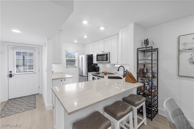 kitchen featuring sink, a breakfast bar, appliances with stainless steel finishes, white cabinets, and kitchen peninsula