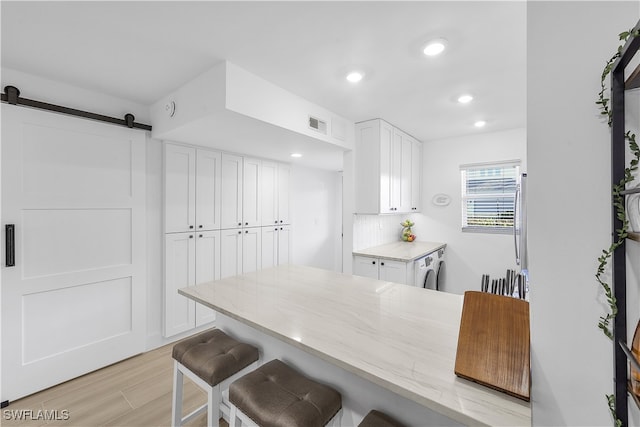 kitchen featuring a breakfast bar, white cabinetry, a barn door, light stone countertops, and backsplash