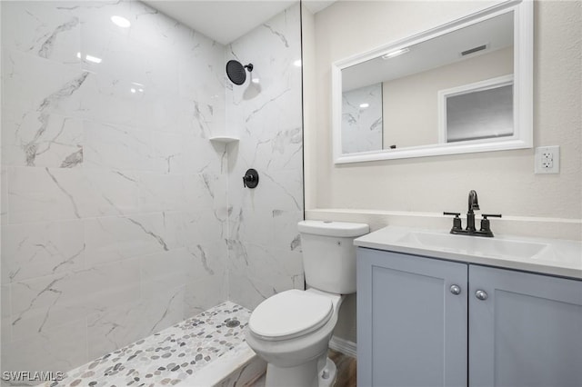 bathroom with a tile shower, vanity, and toilet