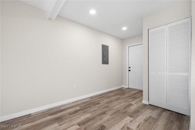 unfurnished bedroom with a closet, beam ceiling, electric panel, and light hardwood / wood-style flooring