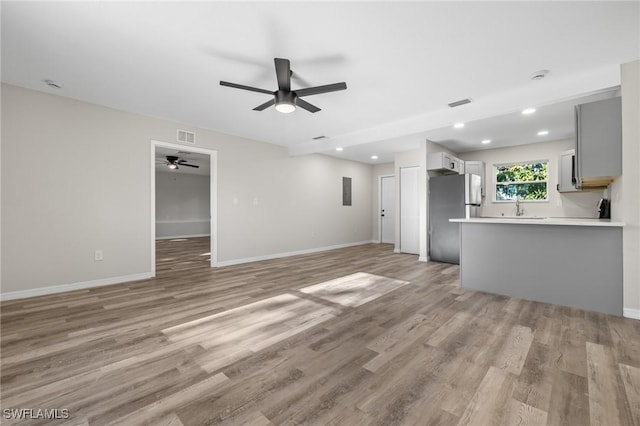 unfurnished living room with ceiling fan, light hardwood / wood-style flooring, and sink