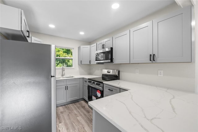 kitchen featuring gray cabinetry, sink, stainless steel appliances, light stone counters, and light wood-type flooring