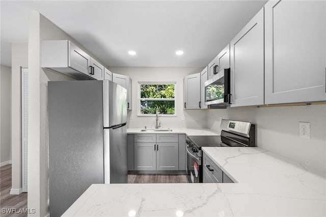 kitchen with light stone countertops, stainless steel appliances, sink, gray cabinets, and dark hardwood / wood-style floors