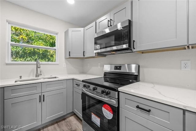 kitchen with sink, dark hardwood / wood-style floors, gray cabinets, light stone countertops, and stainless steel appliances