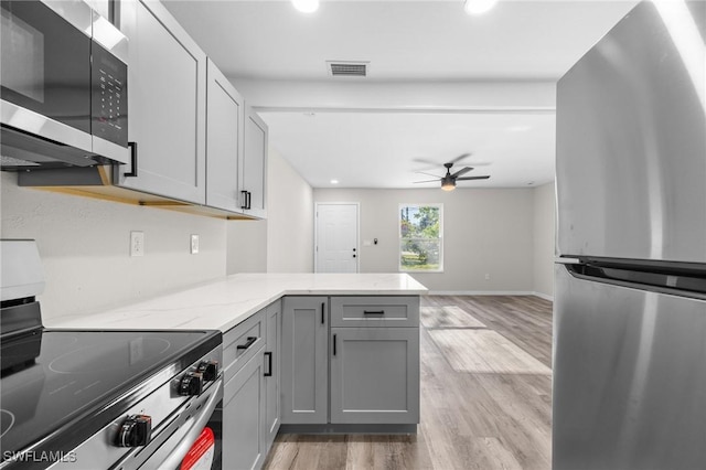 kitchen with gray cabinetry, light stone countertops, light wood-type flooring, appliances with stainless steel finishes, and kitchen peninsula