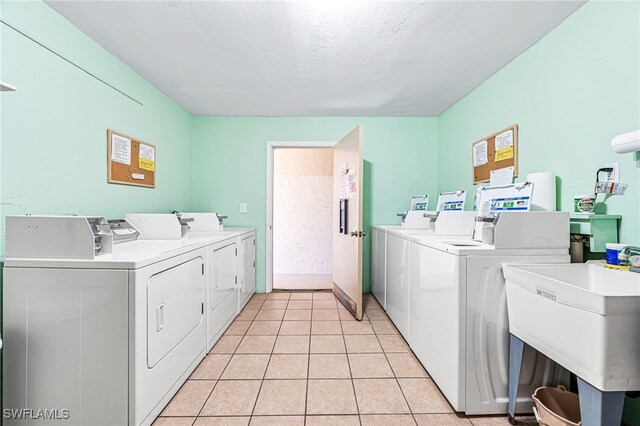 clothes washing area featuring light tile patterned flooring, separate washer and dryer, sink, and a textured ceiling