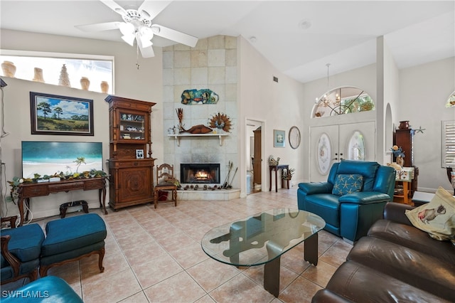 tiled living room featuring ceiling fan with notable chandelier, a fireplace, and high vaulted ceiling