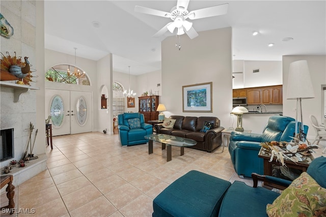 living room with a fireplace, ceiling fan with notable chandelier, high vaulted ceiling, and light tile patterned flooring