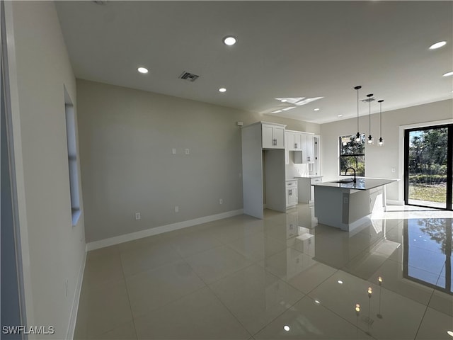 kitchen featuring sink, light tile patterned floors, decorative light fixtures, a center island with sink, and white cabinets