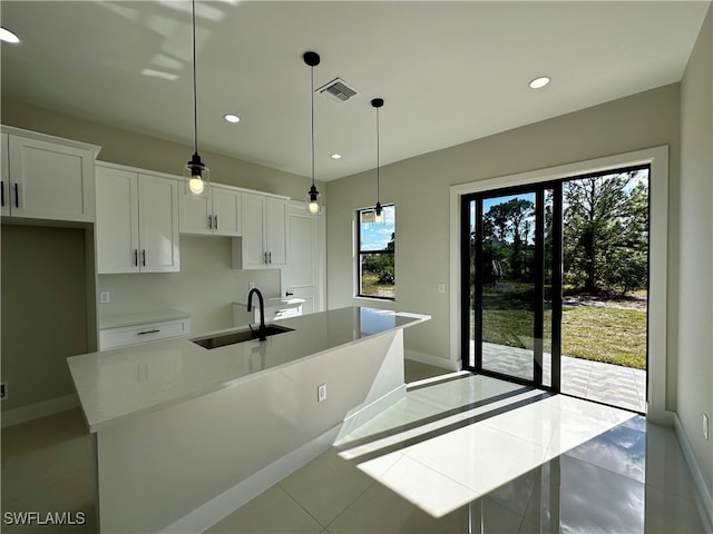 kitchen with white cabinets, decorative light fixtures, a center island with sink, and sink