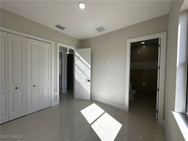 unfurnished bedroom featuring ensuite bath, a closet, and light tile patterned floors