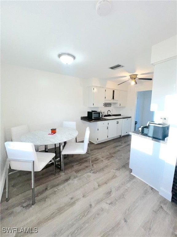 dining space with ceiling fan, light wood-type flooring, and sink