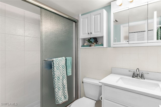 bathroom featuring backsplash, toilet, vanity, a shower with shower door, and tile walls