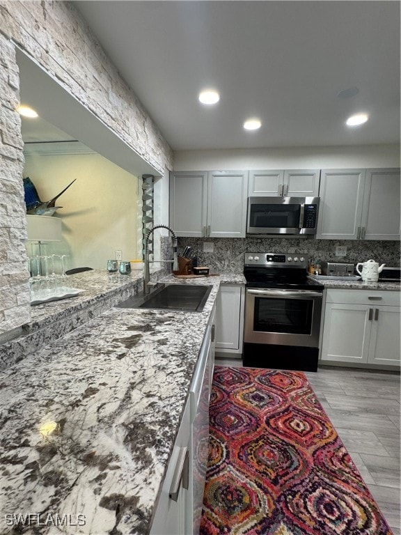 kitchen featuring sink, light hardwood / wood-style flooring, tasteful backsplash, light stone counters, and stainless steel appliances