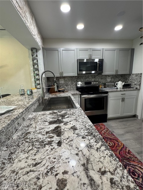 kitchen with light stone countertops, sink, stainless steel appliances, light hardwood / wood-style flooring, and backsplash