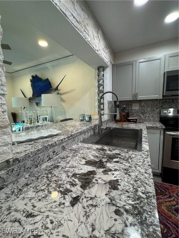 kitchen with light stone countertops, backsplash, stainless steel appliances, crown molding, and sink