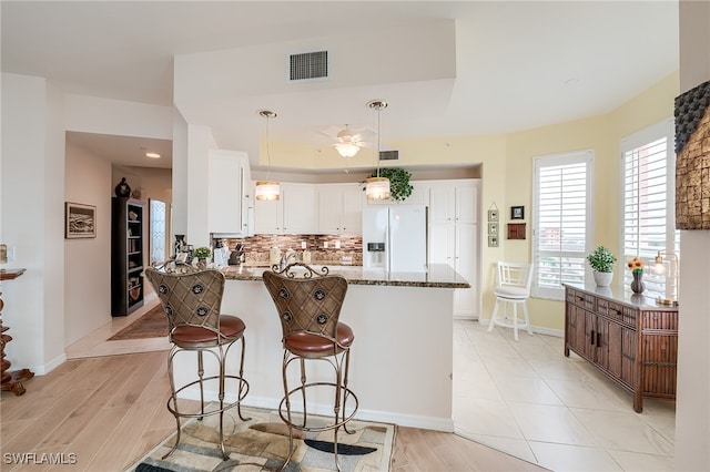 kitchen with white cabinetry, light wood-type flooring, white fridge with ice dispenser, and stone counters