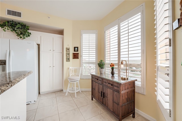 kitchen featuring white refrigerator with ice dispenser, dark brown cabinets, light tile patterned floors, and a healthy amount of sunlight